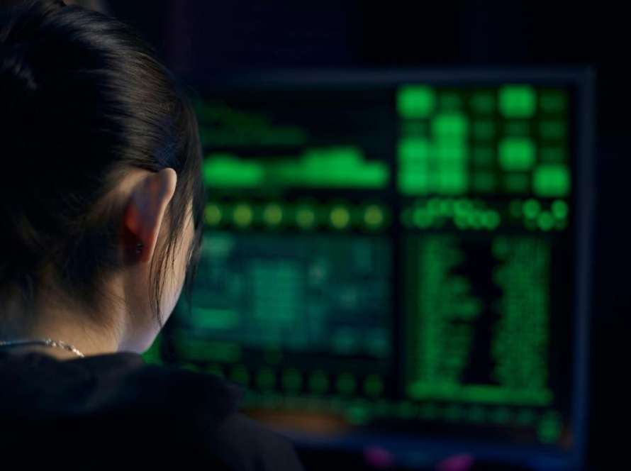 Cyber security consultant reviewing threat data on monitor in dark office