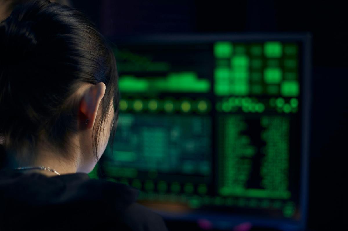 Cyber security consultant reviewing threat data on monitor in dark office